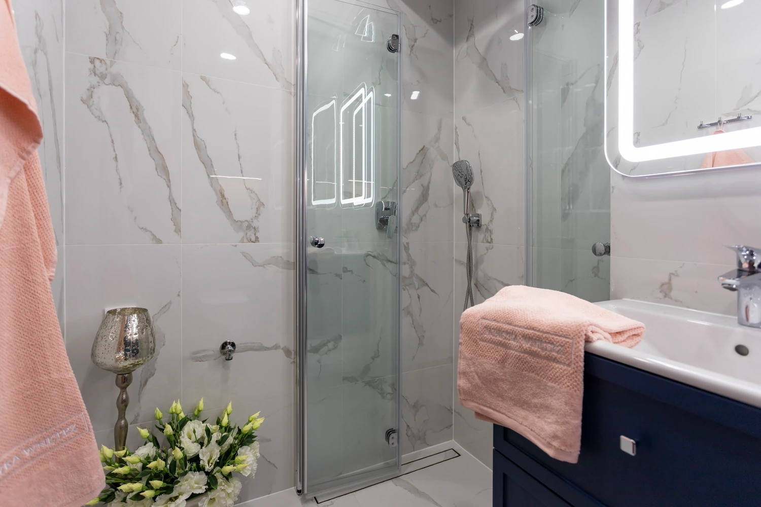 Prysznic walk-in i granatowa szafka z pudrowymi ręcznikami w łazience wykończonej marmurem Calacatta.