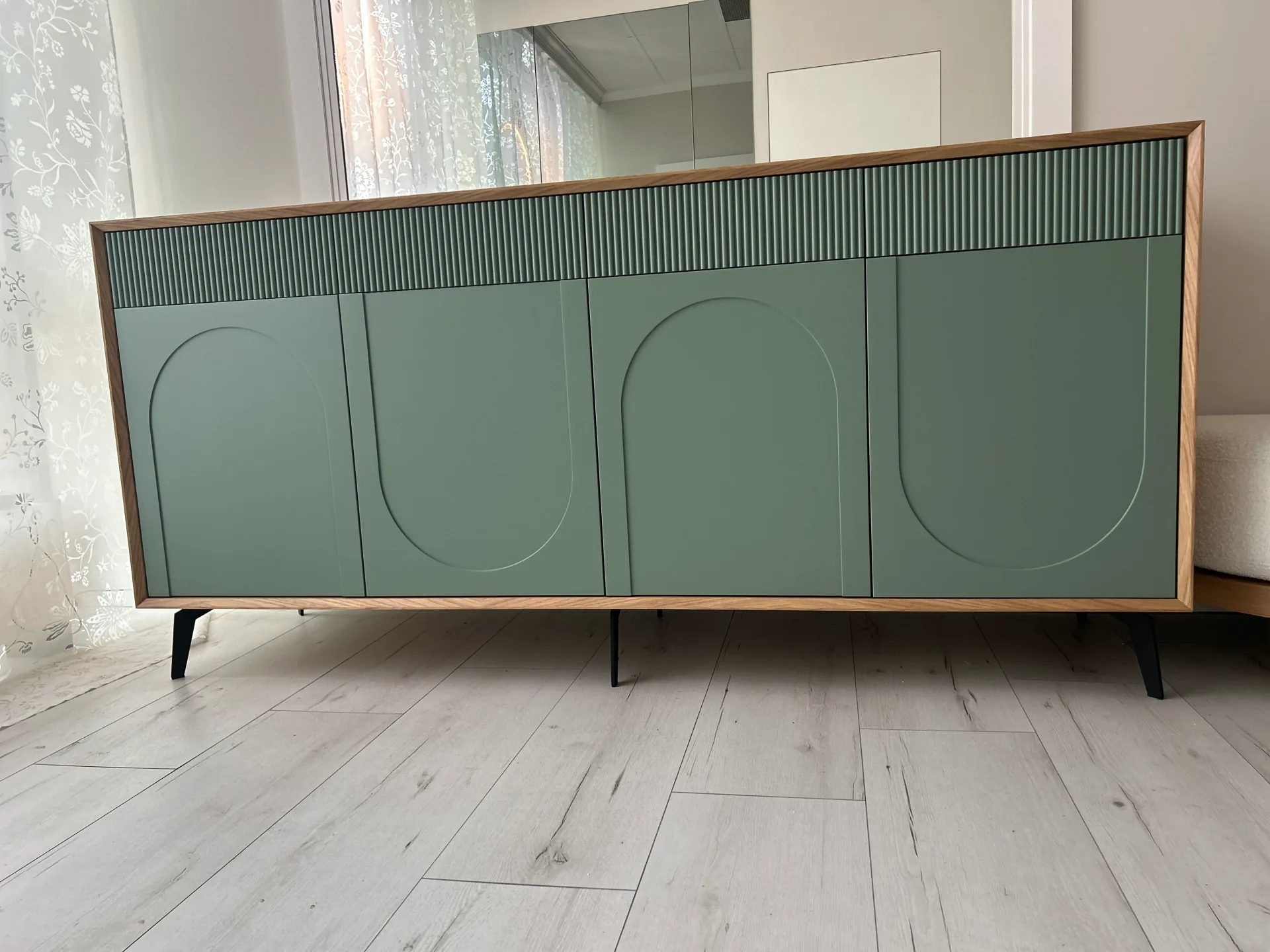 Niska szafka sideboard na wymiar sfotografowana od frontu, z czterema szałwiowymi frontami z wyfrezowanymi łukami, górnym pasem lameli i dębową ramą, na rozstawionych czarnych nóżkach.