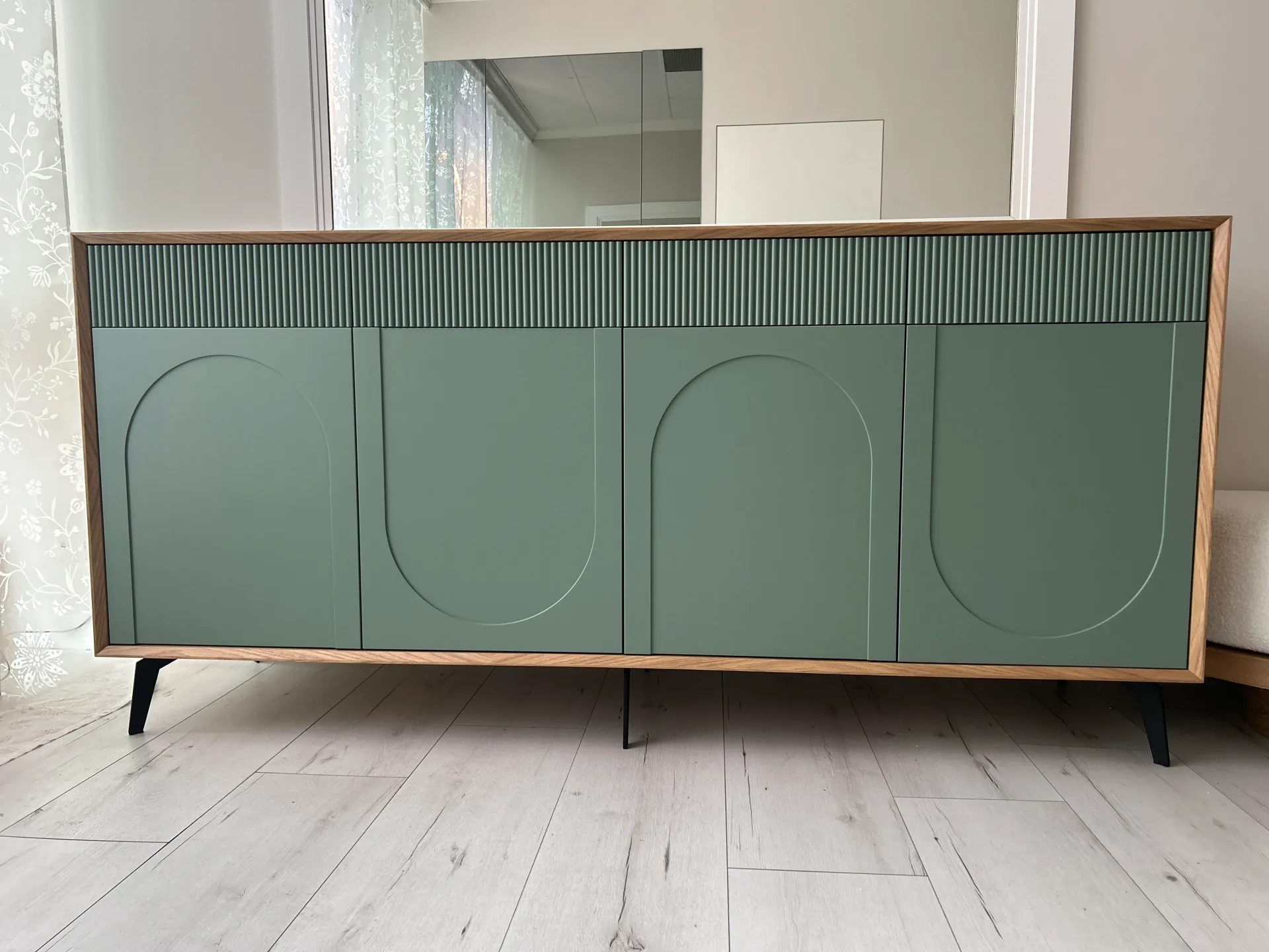 Niska szafka sideboard na wymiar z szałwiowymi frontami z wyfrezowanymi łukami i górnym pasem lameli w dębowej ramie, na czarnych nóżkach, ustawiona pod dużym lustrem.