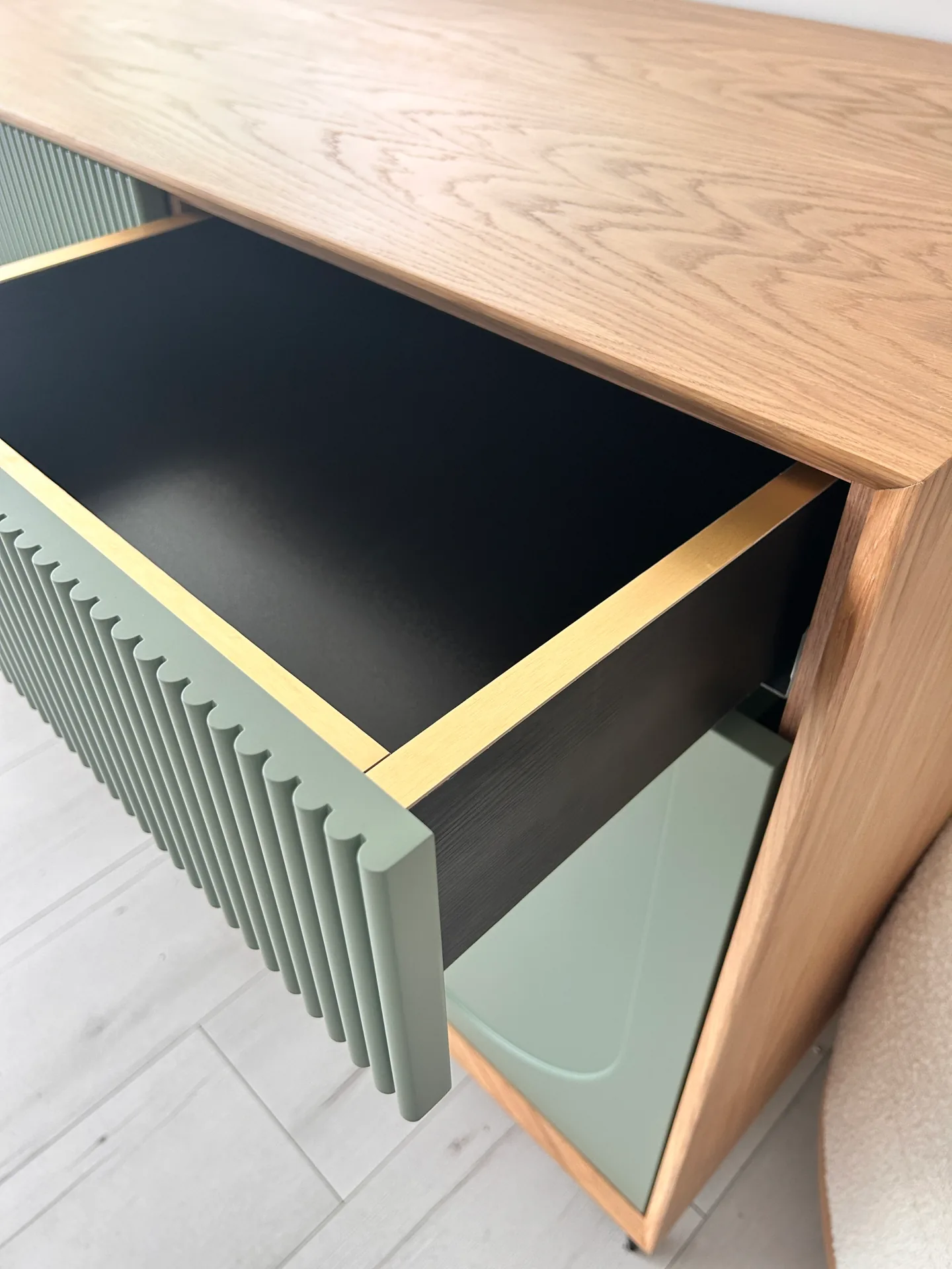 Niska szafka sideboard na wymiar z otwartą szufladą o szałwiowym lamelowym froncie, czarnym dnem i dębowych ściankach, zwieńczona dębowym blatem o ciepłym usłojeniu.